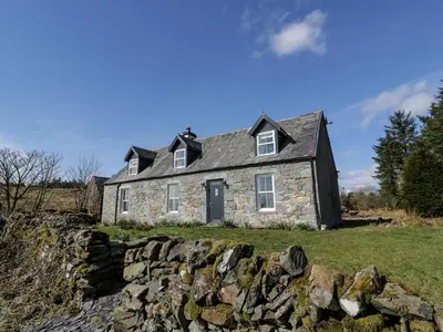 a stone house on a hill with a stone wall at Corrafeckloch Forest Cottages in Bargrennan