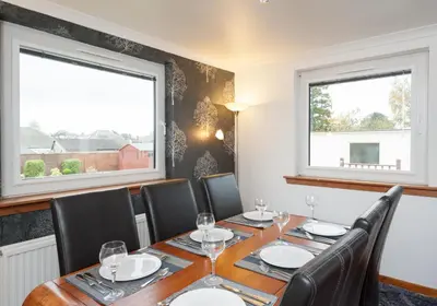 a dining room with a table and chairs and two windows at The Traquair Park Residence in Edinburgh