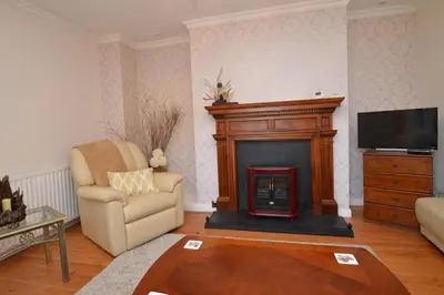 a living room with a fireplace and a chair at Cedar Cottage in Dunoon