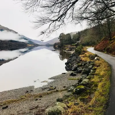 a body of water next to a road next to a lake at Woodside Logcabin Ardoch Lodge in Strathyre
