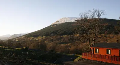a small red house in front of a mountain at Balquhidder Braes Holiday Park Lodges, mostly with Hot Tubs and pet friendly, EV facilities in Lochearnhead