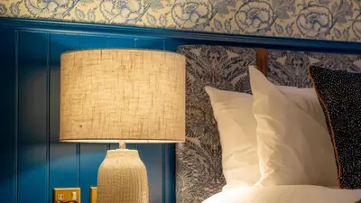 a bedroom with a bed with a blue headboard and a lamp at Brisbane House Hotel in Largs