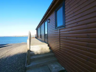 a wooden building with stairs next to the water at Chalet Loch Leven Lodge by Interhome in Ballingry