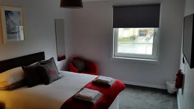 a bedroom with a bed with a window and a red chair at Newtown Apartments in Boʼness