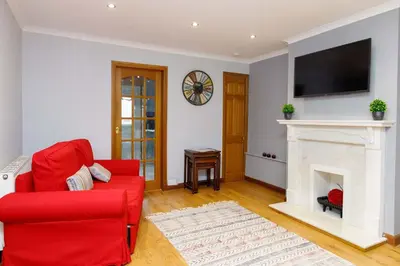 a living room with a red chair and a fireplace at Lomond Serviced Apartments- Inglewood in Alloa
