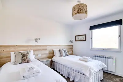 two twin beds in a room with a window at Gamekeeper Lodge loch and mountain view free wifi in Crianlarich