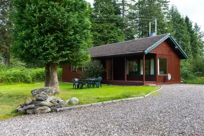 a small red cabin with a tree in front of it at Kestrel Lodge with mountain view free wifi in Crianlarich