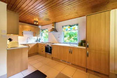 a large kitchen with wooden cabinets and a window at Kestrel Lodge with mountain view free wifi in Crianlarich
