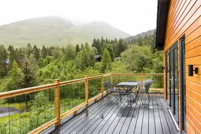 a wooden deck with a table and chairs on it at Stunning 5 star lodge with loch and mountain views in Crianlarich