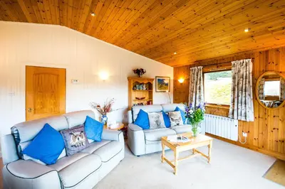 a living room with two couches and a table at Raven Lodge with beautiful views of Loch Dochart in Crianlarich