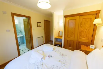 a bedroom with a white bed and a bathroom at Raven Lodge with beautiful views of Loch Dochart in Crianlarich