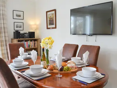 a dining room table with chairs and a television at Invernoe Cottage in Taynuilt
