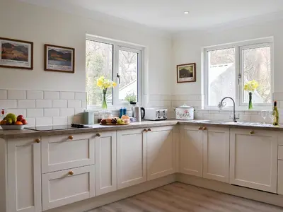 a white kitchen with white cabinets and windows at Invernoe Cottage in Taynuilt