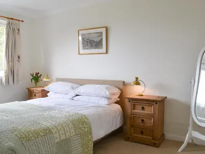a bedroom with a bed with white sheets and a nightstand at Invernoe Cottage in Taynuilt