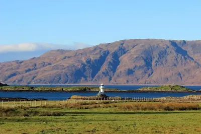 a lighthouse in the middle of a lake with mountains at Lurach House in Port Appin