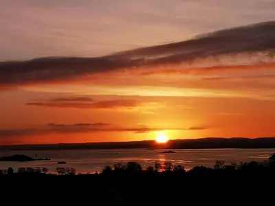 a sunset over a body of water with the sun setting at Bay and Bridge near Edinburgh in Dunfermline