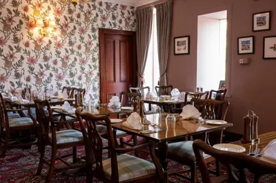 a dining room with tables and chairs and a floral wallpaper at Knipoch House Hotel in Oban