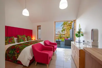 a bedroom with a large bed and two pink chairs at Ardtorna in Benderloch