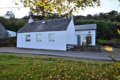 a white house on the side of a road at Gate Cottage in Tighnabruaich
