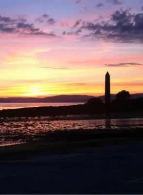 a sunset on the beach with a lighthouse in the distance at Largs stay With Private parking in Largs