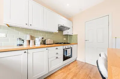 a kitchen with white cabinets and a wooden floor at Three Bed Holiday Home in Glasgow in Glasgow