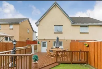 a house with a wooden deck with a table and chairs at Silverburn new house with free parking and nice garden in Glasgow