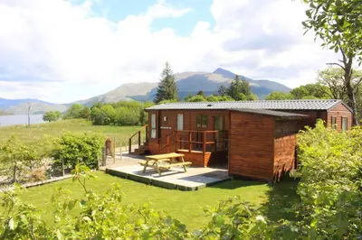 a small cabin in a field with mountains in the background at Mountain View in Taynuilt