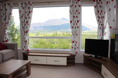 a living room with a large window and a television at Glen View in Taynuilt