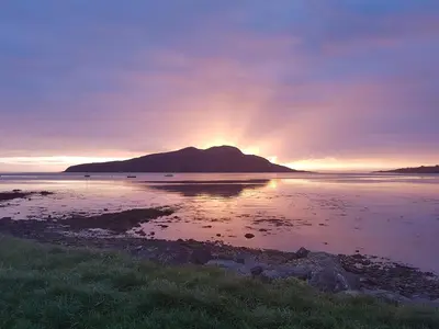 a sunset over a body of water with a mountain at Glenisle Cottage in Lamlash