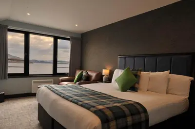 a bedroom with a large bed and a couch and windows at The Lodge On Loch Lomond Hotel in Luss