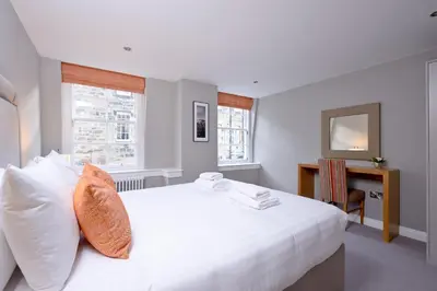 a white bedroom with a large white bed with an orange pillow at Destiny Scotland New Town Apartments in Edinburgh