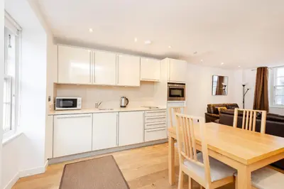 a kitchen and dining room with white cabinets and a wooden table at JOIVY Superb Flats in the Heart of Edinburgh in Edinburgh