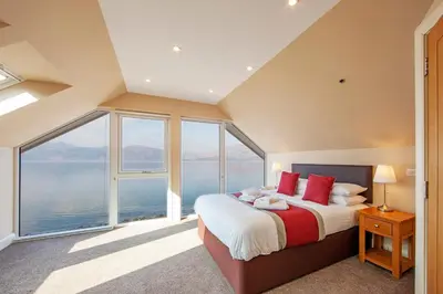 a bedroom with a large bed and large windows at Beach Houses with Hot Tubs in Glencoe