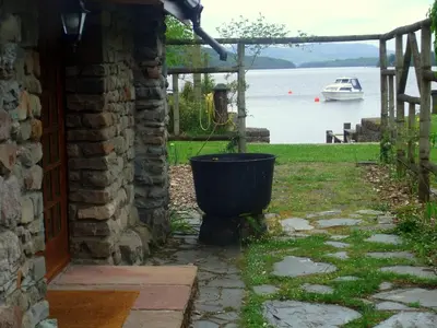 a bucket outside of a house with a boat in the water at Loch Lomond shore Boat House in Balmaha