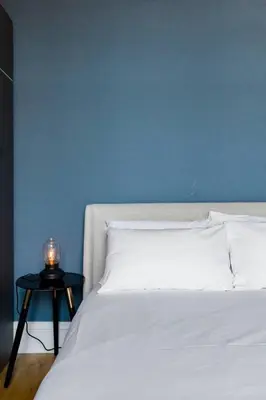 a bed with a blue wall and a table with a lamp at Incredible contemporary flat in heart of west end in Glasgow