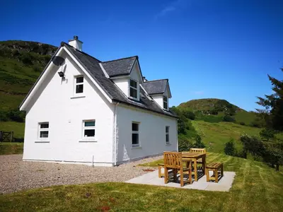 a white house with a table and two benches at Achalic Beag in Lerags