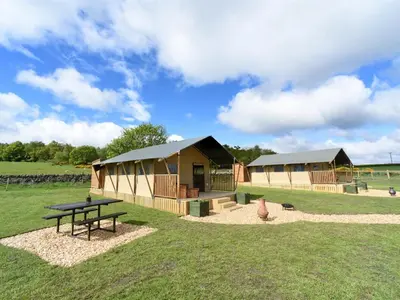 a couple of huts in a field with a picnic table at Carr's Hill Luxury Safari Tents in Denny