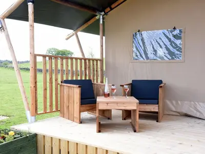 a patio with two chairs and a table on a deck at Carr's Hill Luxury Safari Tents in Denny
