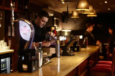 a man standing at a bar preparing a glass of wine at Dalziel Park Hotel in Motherwell
