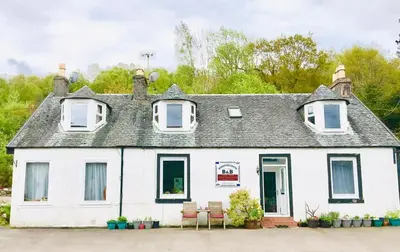a white house with chairs in front of it at Rowantreebank Bed and Breakfast in Arrochar