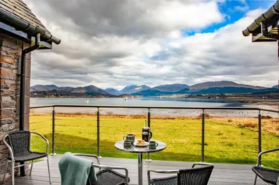 a table and chairs on a balcony with a view of a lake at Seabank House in Oban