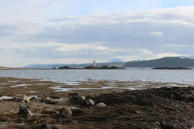 a rocky beach with a lighthouse in the distance at Sealladh in Port Appin