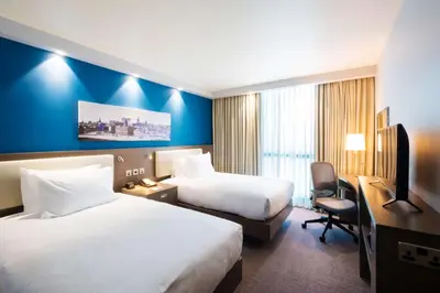 a hotel room with two beds and a desk at Hampton By Hilton Hamilton Park in Hamilton