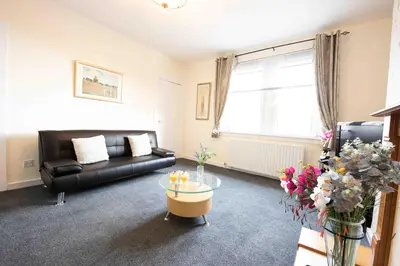 a living room with a black couch and a glass table at PREMIER - Garfield House in Bellshill