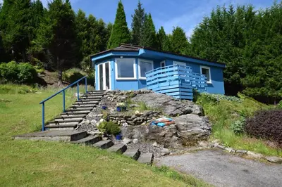a blue house sitting on top of a rock at Byron Cottage overlooking Loch Goil in Lochgoilhead
