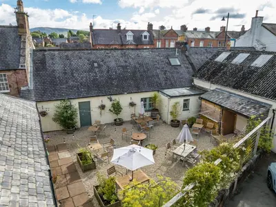 an outdoor patio with tables and chairs and an umbrella at Buccleuch and Queensberry Arms Hotel in Thornhill
