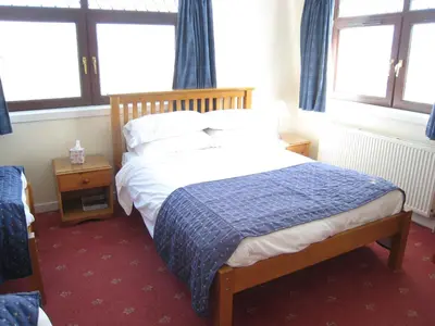 a bedroom with a bed with a blue blanket and two windows at Herdshill Guest House in Wishaw