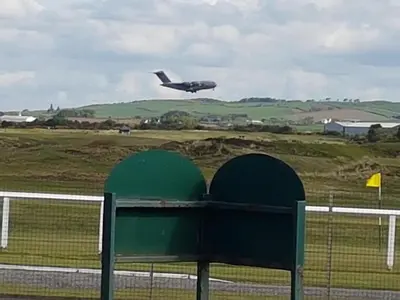 an airplane is flying over a runway with a fence at Fairways Cottages in Prestwick