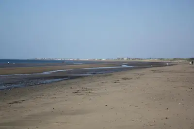 an empty beach with people walking on the sand at Fairways Cottages in Prestwick