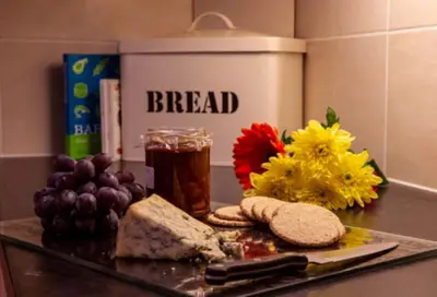 a counter top with bread and a drink and flowers at Bonnie Banks Cottage in Balloch